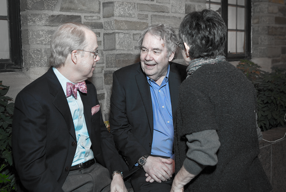 Candid photo of three people in mid conversation with a stone wall behind them. They are wearing business attire and smiling.
