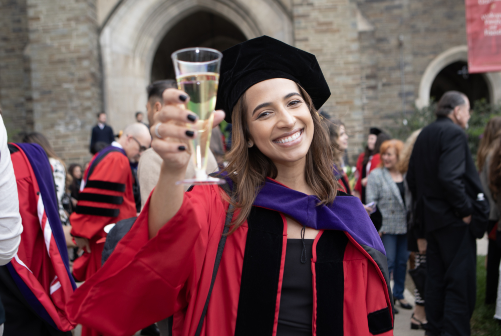 a student in her regalia toasting a glass of champagne