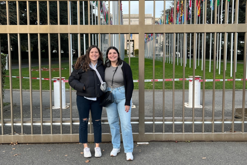 two students outside the gates to the United Nations with a row of flags behind them