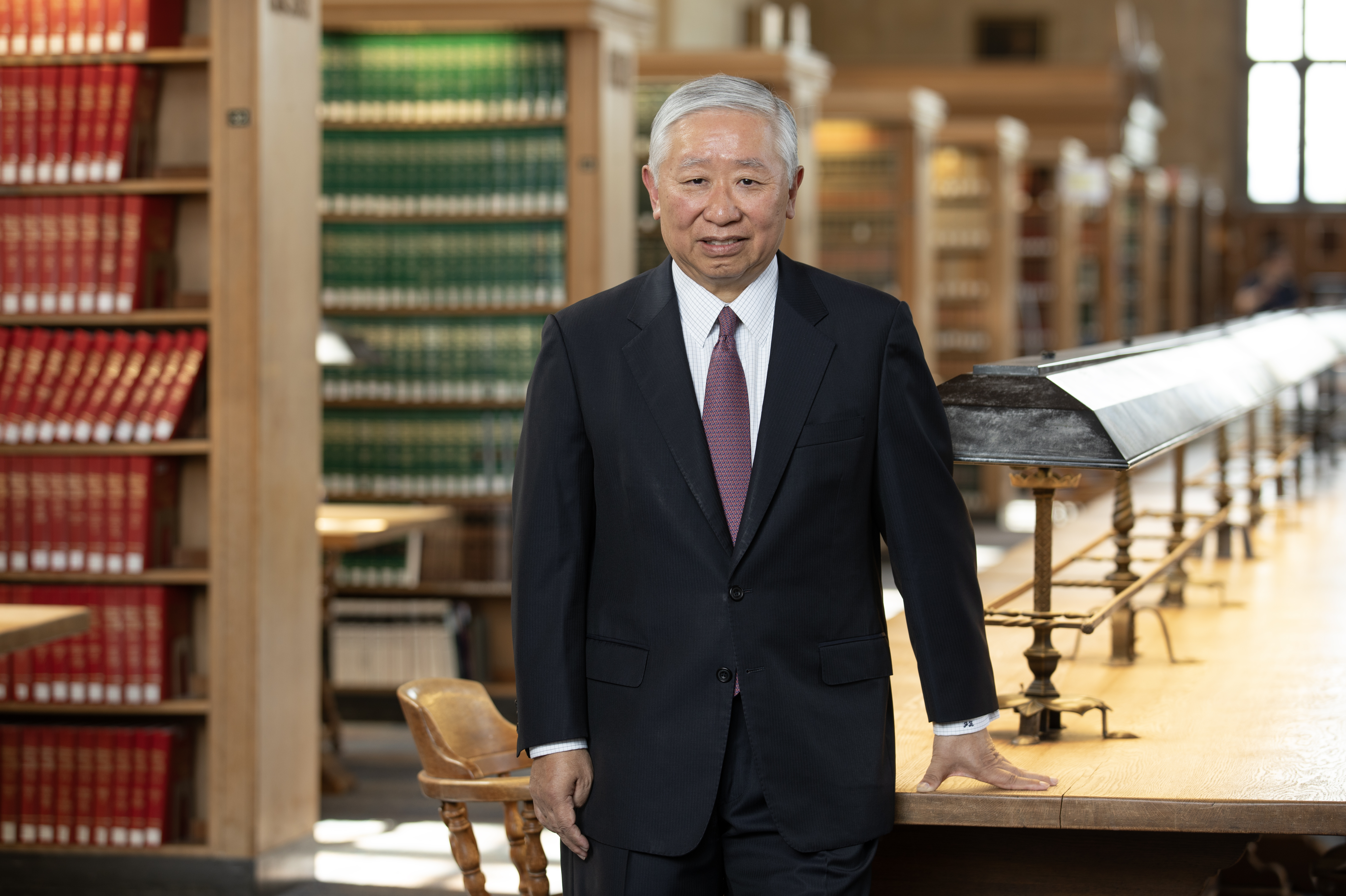 Jonathan Zhu, standing in front of a table in the law school library, wearing a black jacket and red tie