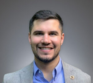 Kevin Sackett on gray background wearing a blue shirt and gray jacket