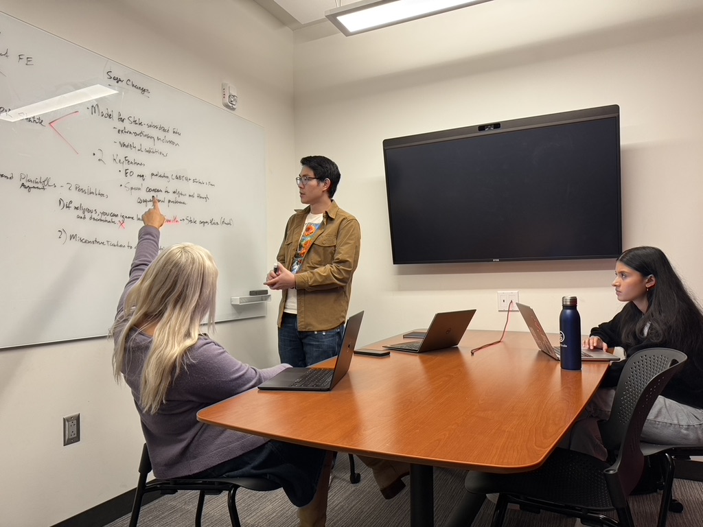 three students discuss materials on a white board