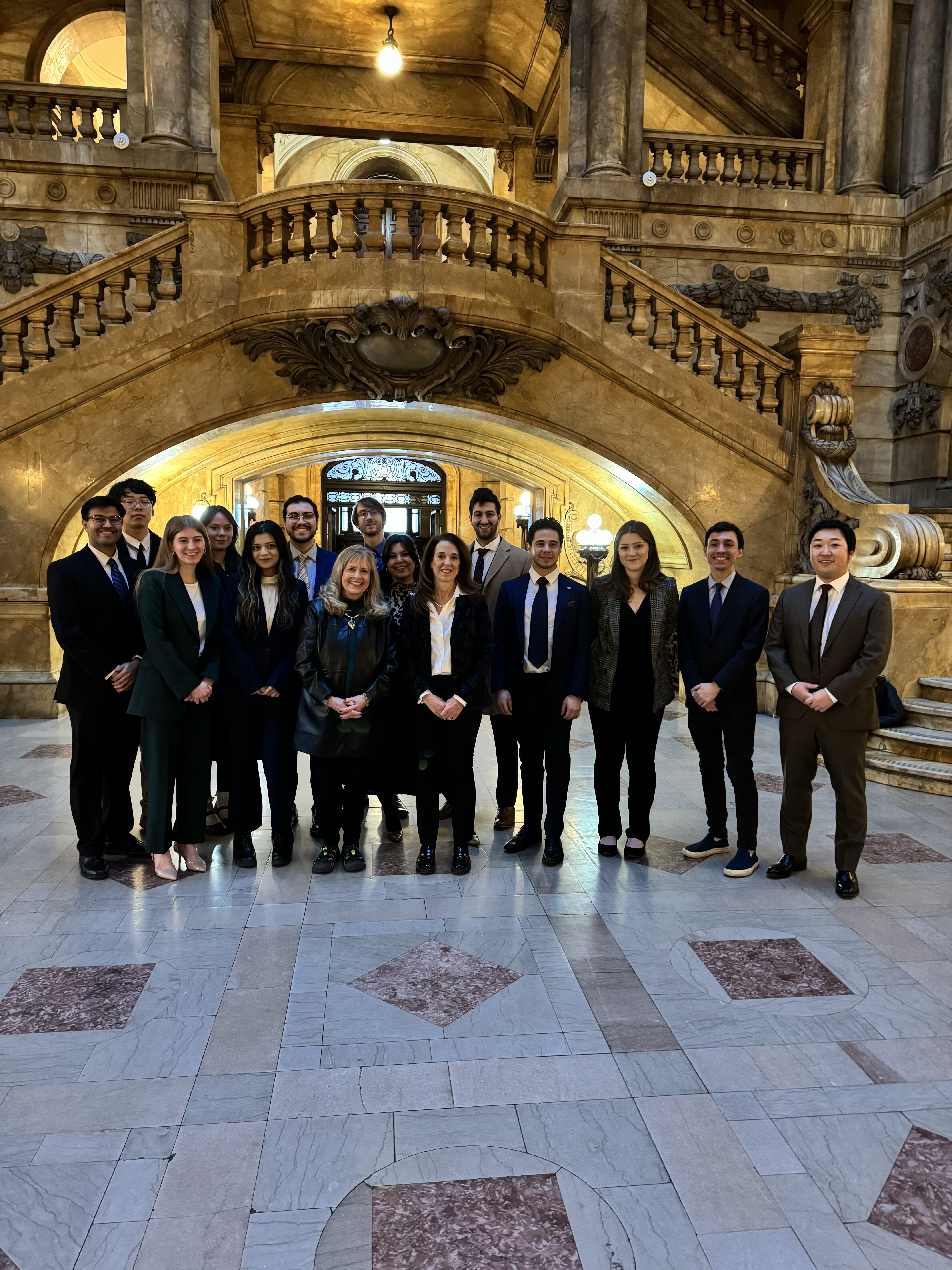 group of students in an ornate lobby with an arched staircase behind them